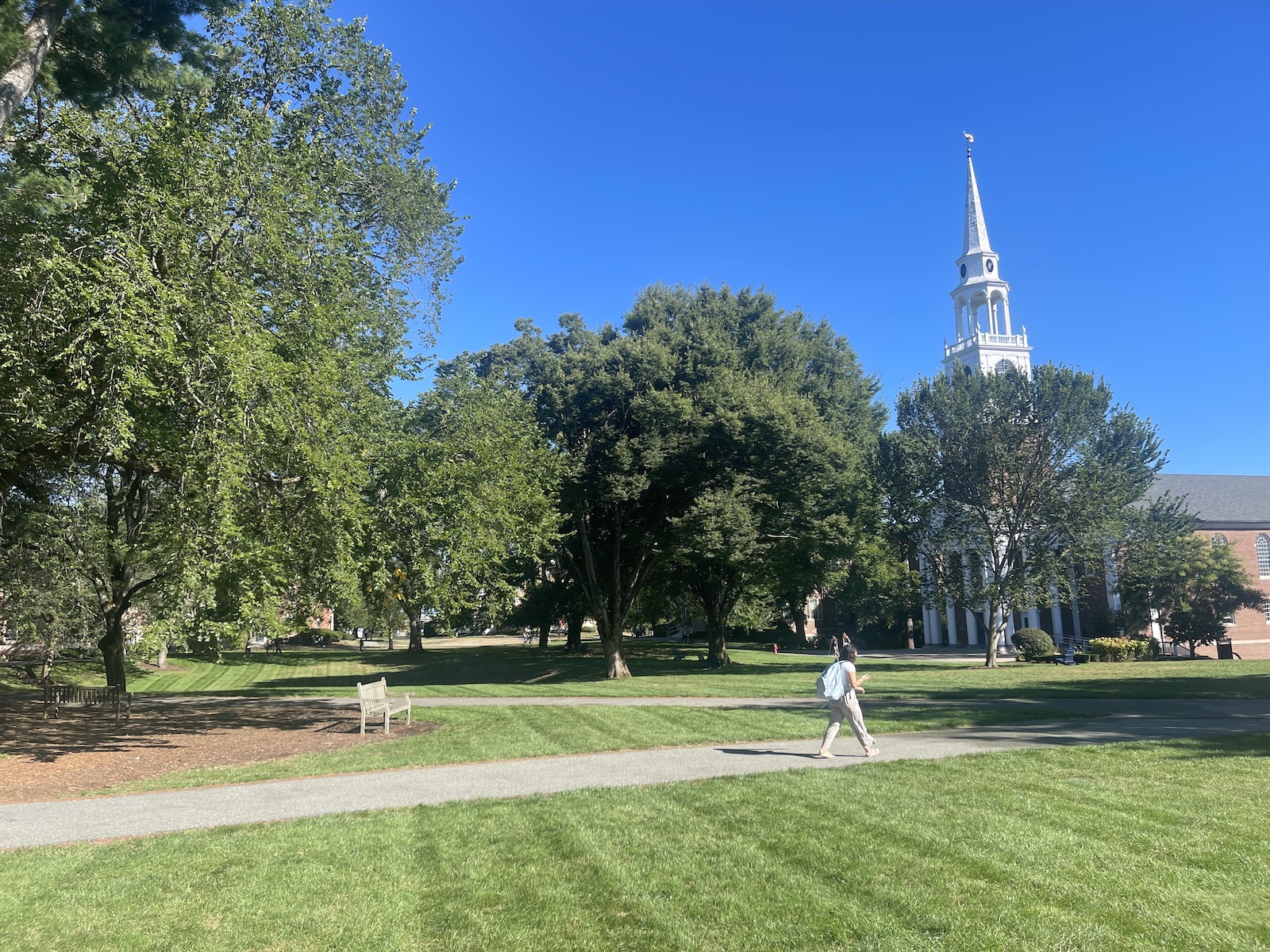 Wheaton College's original brick buildings left and right, the chapple with white spire right; a sprawling green lawn; all in bright late summer morning sun coming from behind.